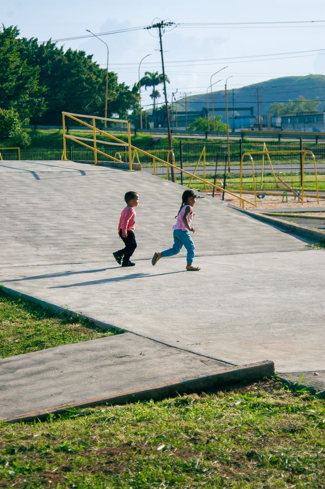 Two children running freely in a park setting in Venezuela, enjoying a sunny day.