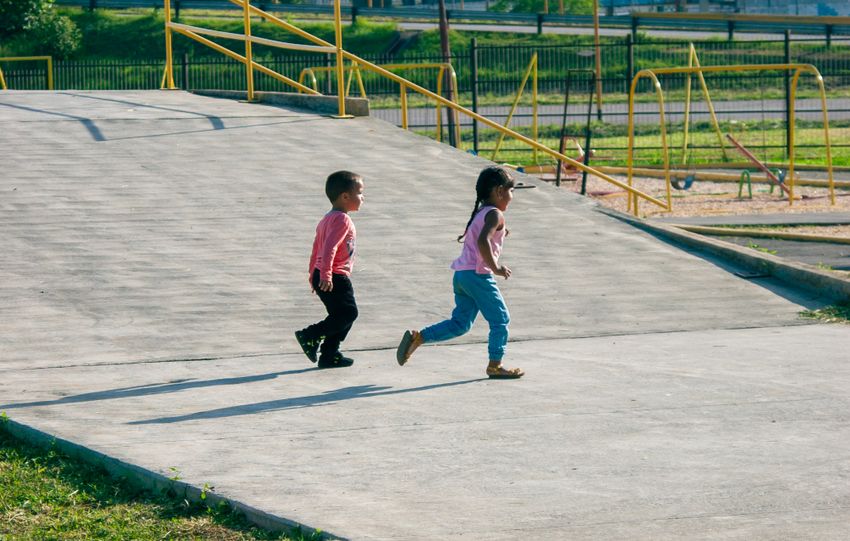 Two children running freely in a park setting in Venezuela, enjoying a sunny day.